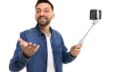 a man on a selfie stick holds a phone and broadcasts, gesturing to the camera with a smile on his face, Concept of online excursions and online training