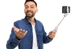 a man on a selfie stick holds a phone and broadcasts, gesturing to the camera with a smile on his face, Concept of online excursions and online training